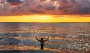 man raising his arms on sea under black clouds